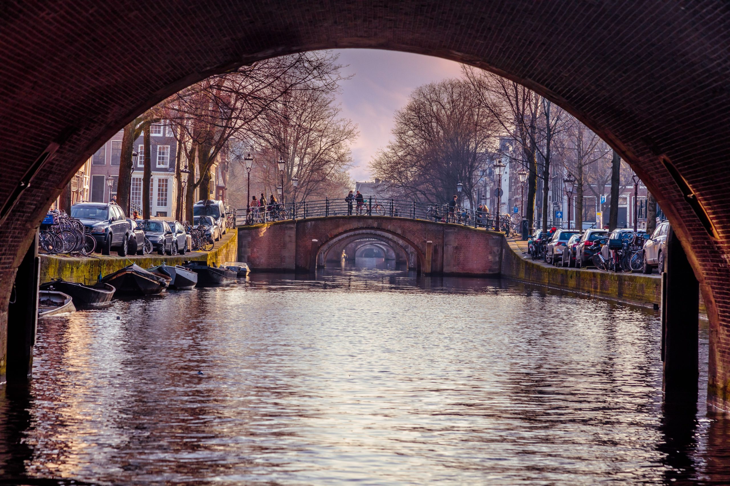 View through a canal tunnel in Amsterdam with bridges and trees.