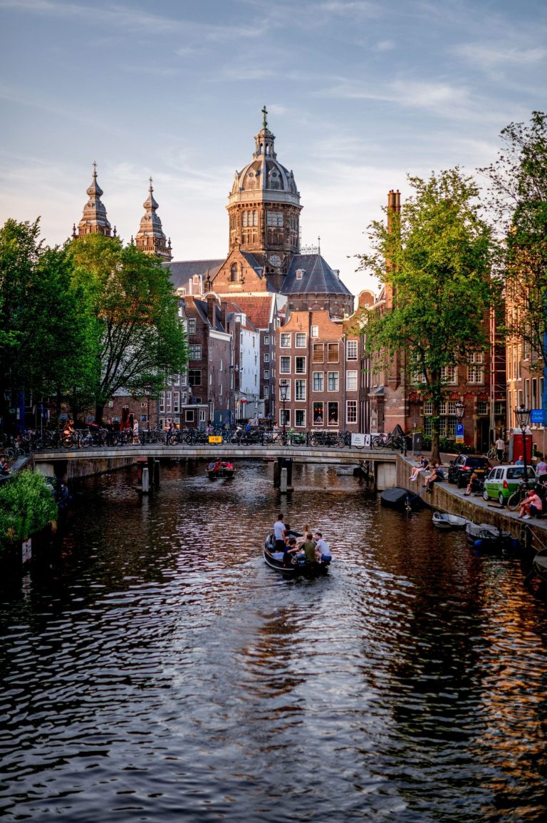 Boat on canal with historic buildings and church tower in background.