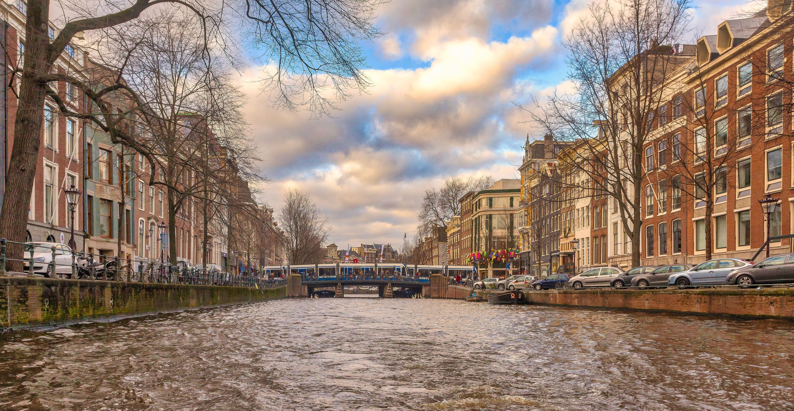 Canal with bridge and buildings on either side under a cloudy sky.