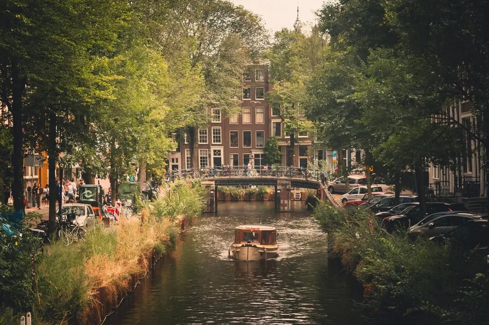 Boat on a canal with trees and buildings in the background.